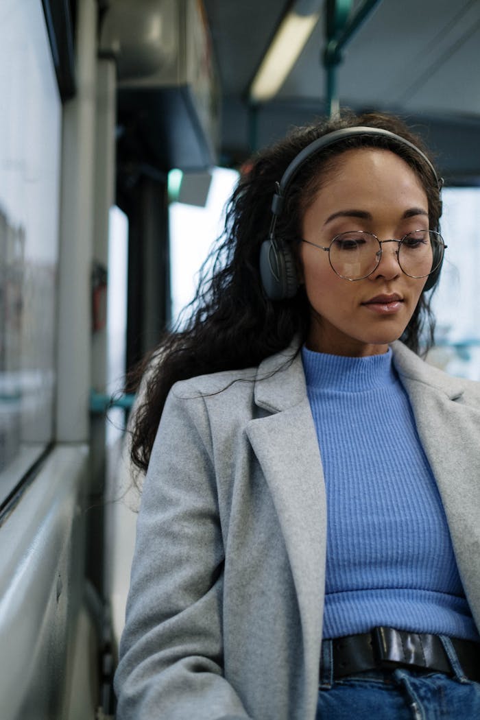 Young woman wearing headphones and eyeglasses, enjoying music on a bus.